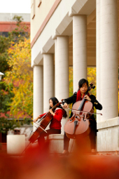 2 students playing cellos on campus